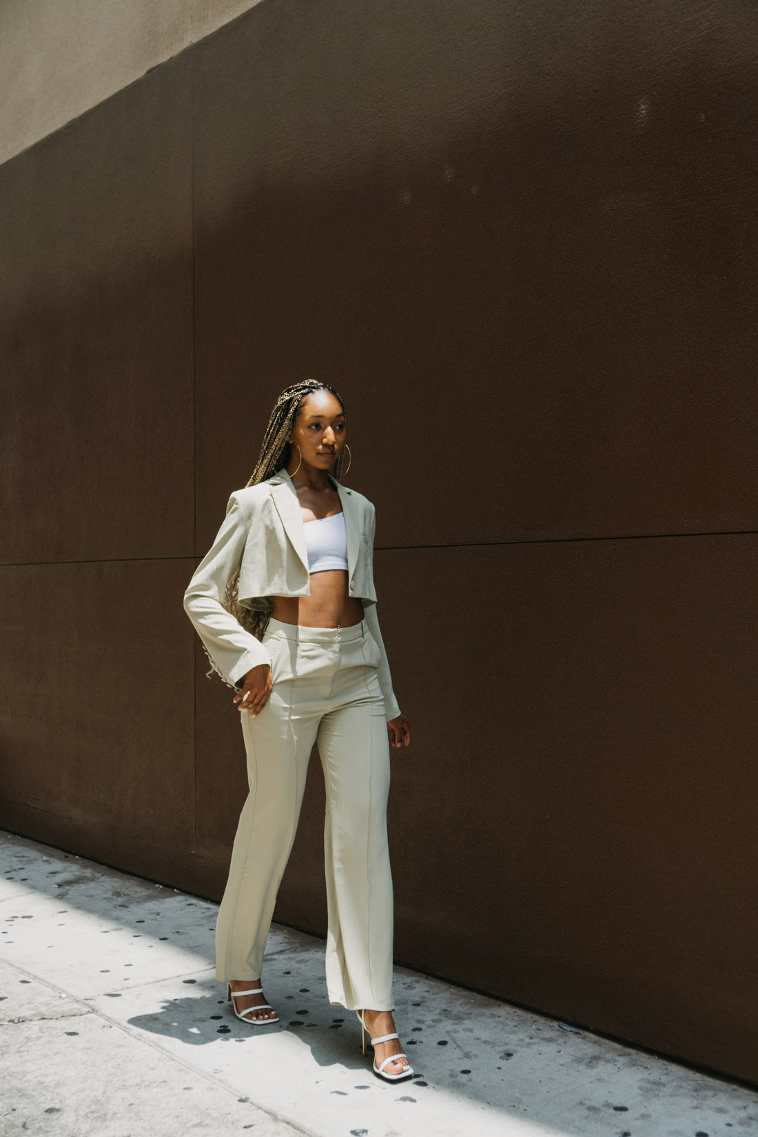 Woman in white minimal linen outfit standing beside a neutral wall